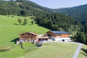 Un chalet à deux étages doté d’un balcon, entouré d’un paysage verdoyant et de collines boisées.