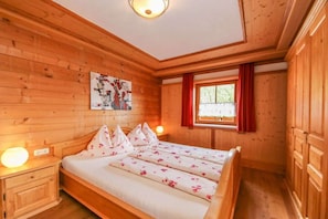Ein Zimmer mit Holzboden, einem Bett, einem Nachttisch, einem Wandbild und einem Fenster mit roten Vorhängen.