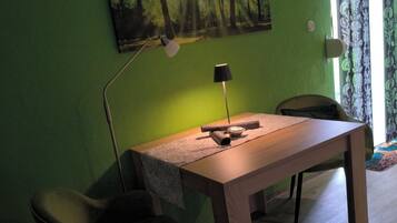 A room with a wooden desk, two chairs, a lamp, and a painting of a forest on the wall.