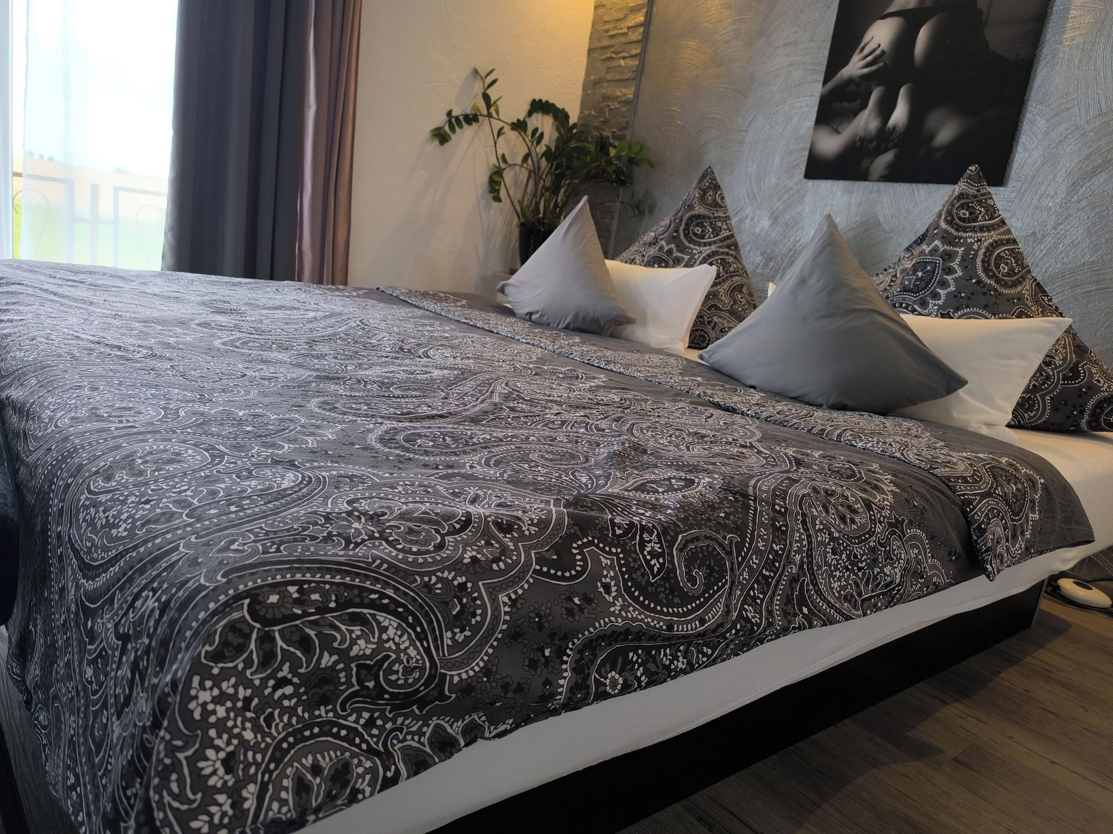 Ein Bett mit einem gemusterten Bettbezug, Kissen und einem an der Wand hängenden Kunstwerk.