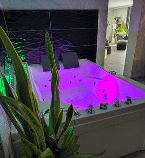 A modern bathroom with a large bathtub, green plants, and a mirror reflecting the room. - Chalet with a sauna, hot tub, and waterbed (Allstedt)