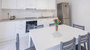 Una cucina moderna con mobili bianchi, un frigorifero in acciaio inossidabile, un tavolo con sedie e un vaso con fiori sul tavolo.