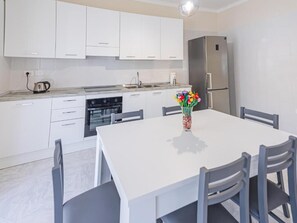 Una cucina moderna con mobili bianchi, un frigorifero in acciaio inossidabile, un tavolo con sedie e un vaso con fiori sul tavolo.