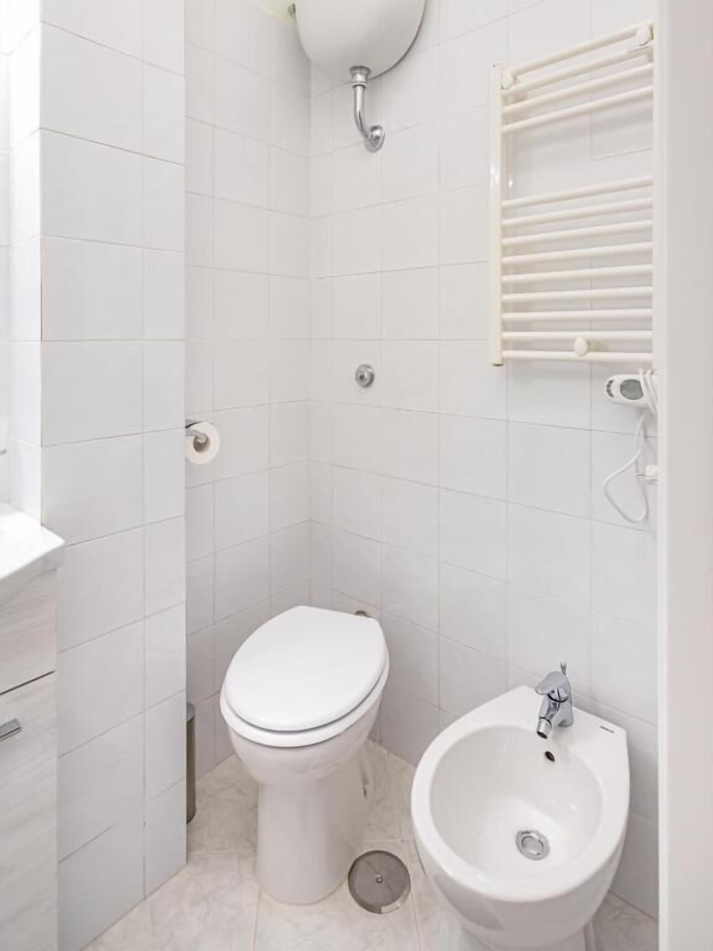 Un bagno piccolo e bianco con un water, un bidet e un appendi asciugamani.