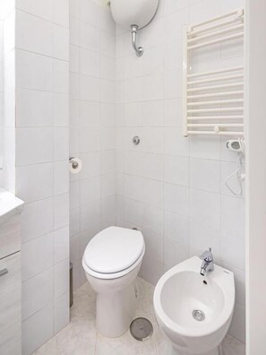 Un bagno piccolo e bianco con un water, un bidet e un appendi asciugamani.