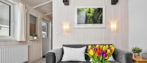 Un salon moderne avec un canapé gris, une table basse ornée d’un vase de tulipes et un tableau encadré accroché au mur.