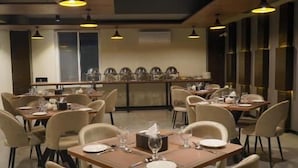 A dining area with multiple tables and chairs, a central bar area, and pendant lighting. - Destination Hotel Gilgit (Gilgit)
