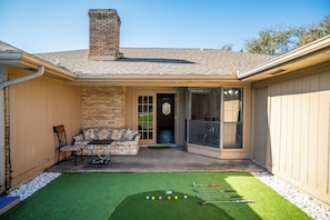 A backyard with a patio, a brick wall, a sliding glass door, and a green artificial turf with golf equipment. - 4BR Carrollton Escape (Carrollton)