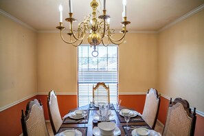 A dining room with a chandelier, wooden chairs, a table set for four, and a window with blinds. - 4BR Carrollton Escape (Carrollton)