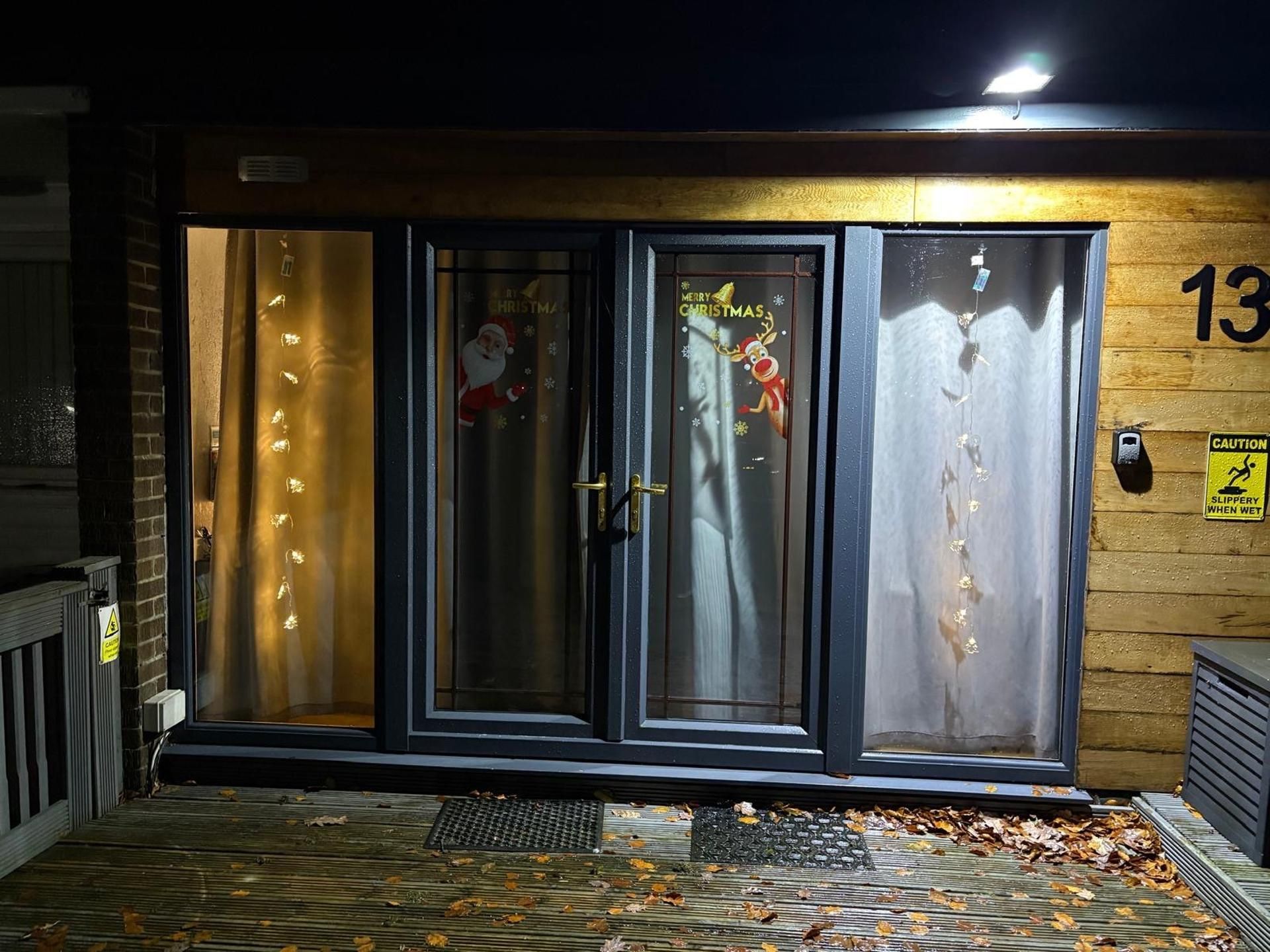 Une entrée d’immeuble avec une porte en verre, une couronne de Noël et un panneau d’avertissement.