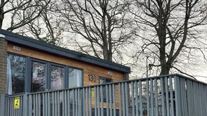 A building with a wooden facade, numbered 138, featuring large windows and a balcony with a metal railing. - Pet Friendly 2-bed Lodge, Sleeps 5, Pool & Parking (Caernarfon)