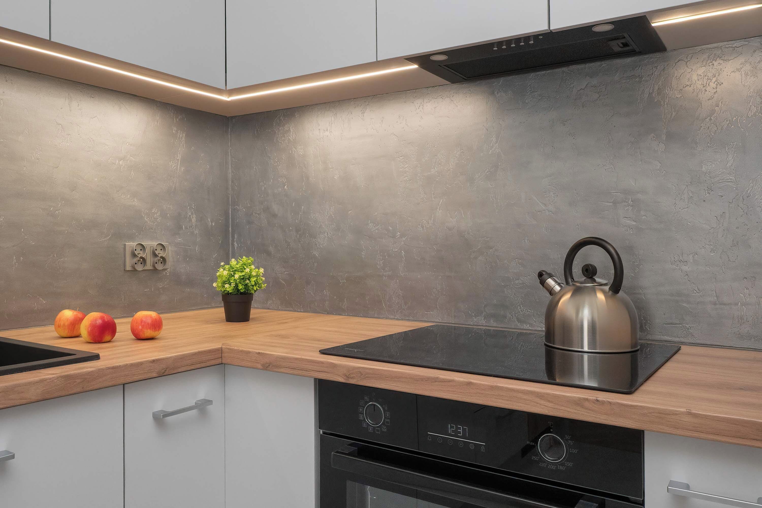 Una cocina moderna con estufa integrada, hervidor y planta en maceta sobre la encimera.