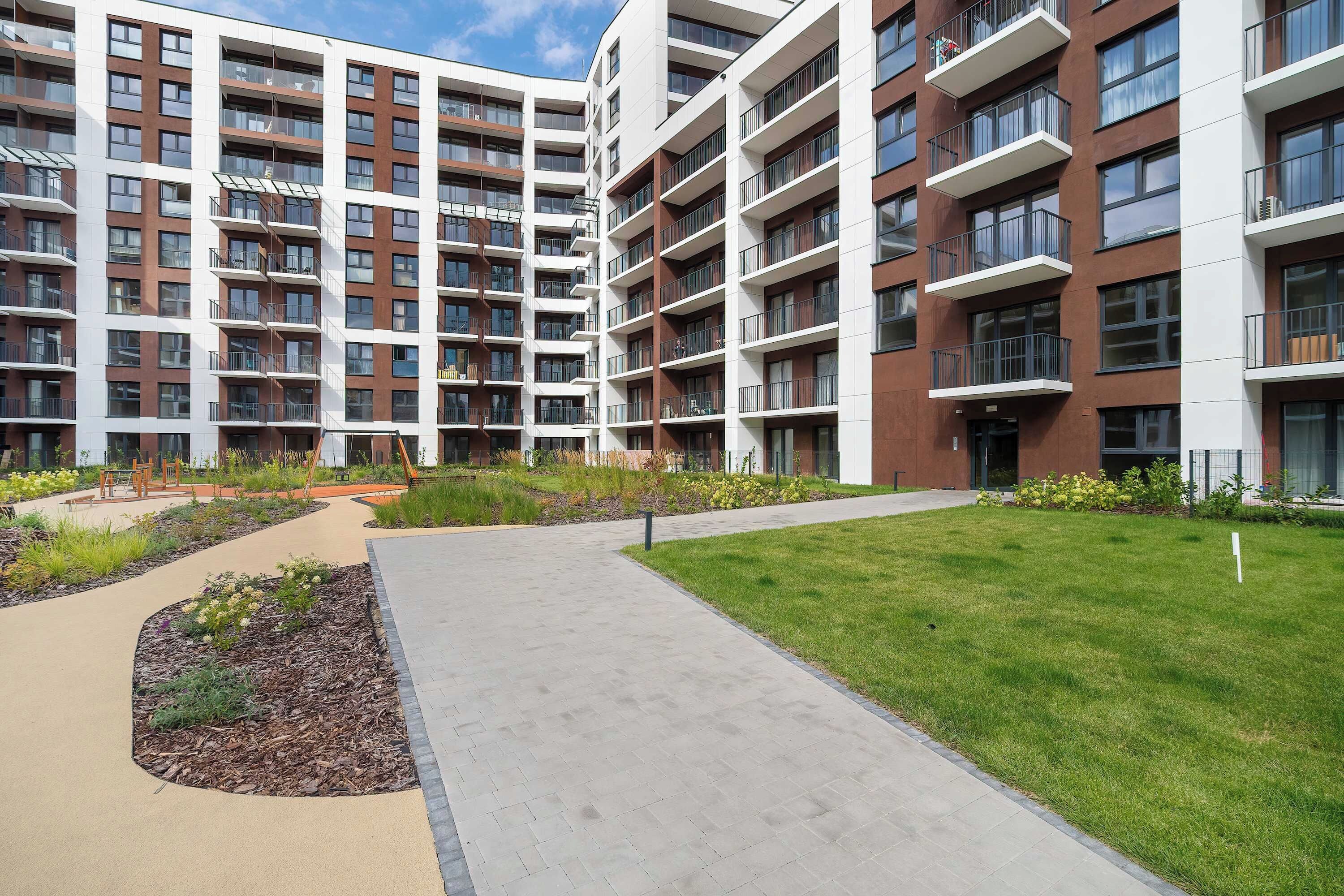 A multi-story residential building with balconies, a landscaped courtyard, and a paved walkway.