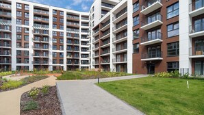 A multi-story residential building with balconies, a landscaped courtyard, and a paved walkway. - Modern Apartment in the City Center | Balcony (Łódź)
