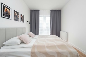 A bedroom with a bed, pillows, a bedside table, a radiator, and curtains. - Modern Apartment in the City Center | Balcony (Łódź)