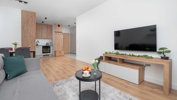 A modern living space with a kitchen, dining area, and a flat-screen TV mounted on the wall. - Modern Apartment in the City Center | Balcony (Łódź)