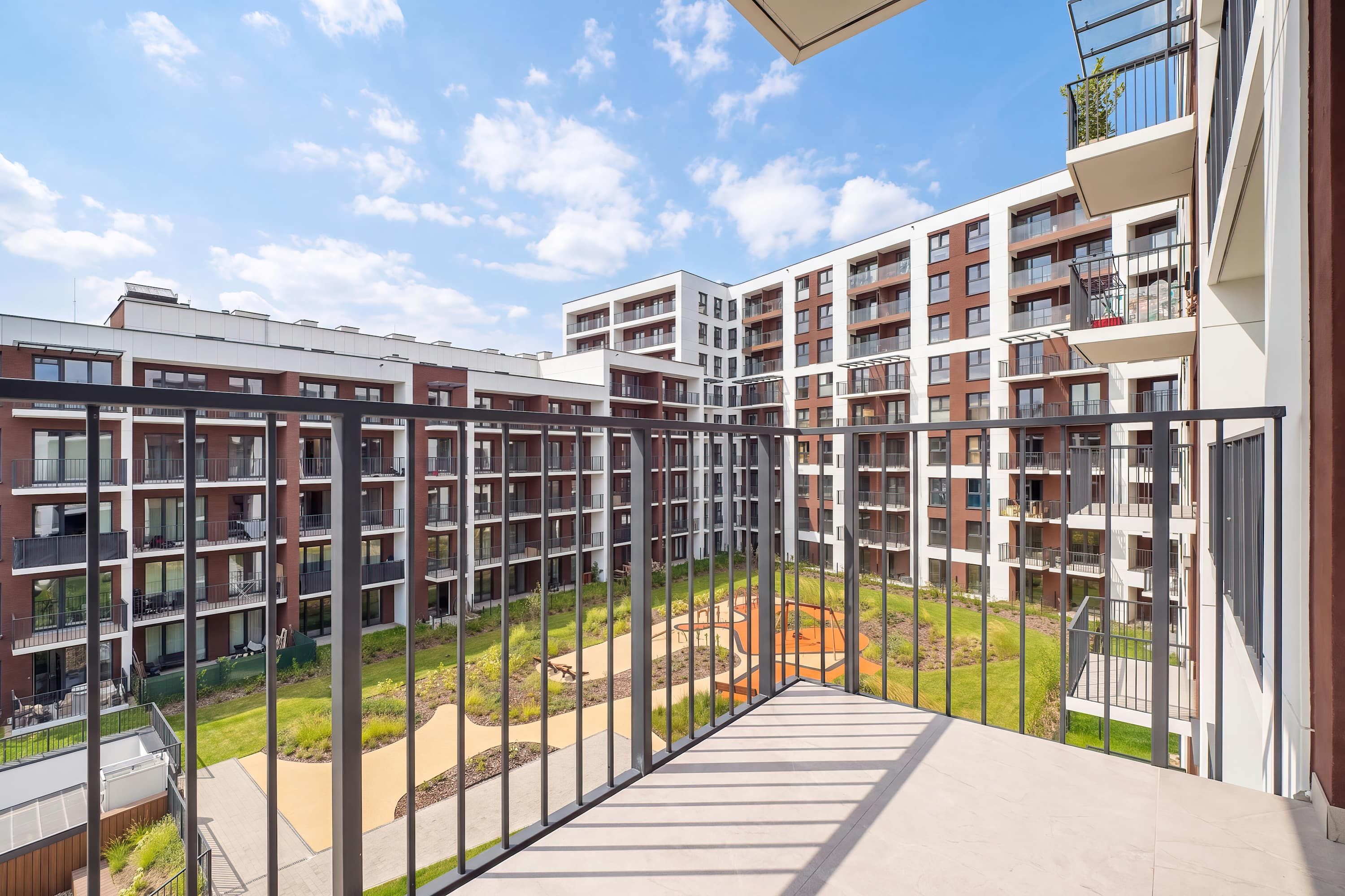 Moderni kerrostalo, jossa on useita parvekkeita, keskeinen sisäpiha ja avoin taivas.