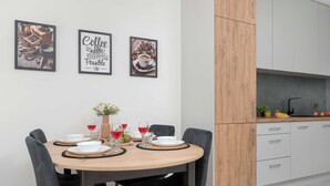 A modern kitchen with white cabinets, a wooden dining table set for four, and three framed coffee-themed pictures on the wall. - Modern Apartment in the City Center | Balcony (Łódź)