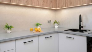 A modern kitchen with a grey countertop, wooden cabinets, a black faucet, and two potted plants. - Modern Apartment in the City Center | Balcony (Łódź)