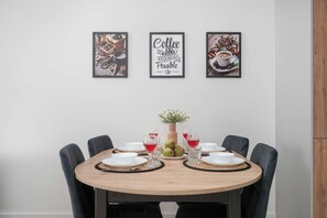 A dining area with a round wooden table, six chairs, and three framed coffee-themed artworks on the wall. - Modern Apartment in the City Center | Balcony (Łódź)