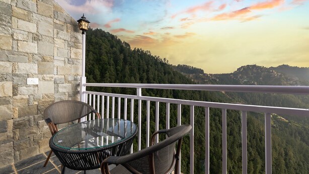 A balcony with a glass table and wicker chairs, overlooking a mountainous landscape.