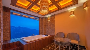 A bathroom with a large bathtub, stone walls, and a view of mountains.