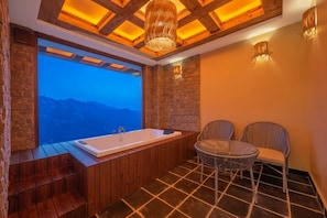 Un baño con una bañera grande, paredes de piedra y vistas a montañas.