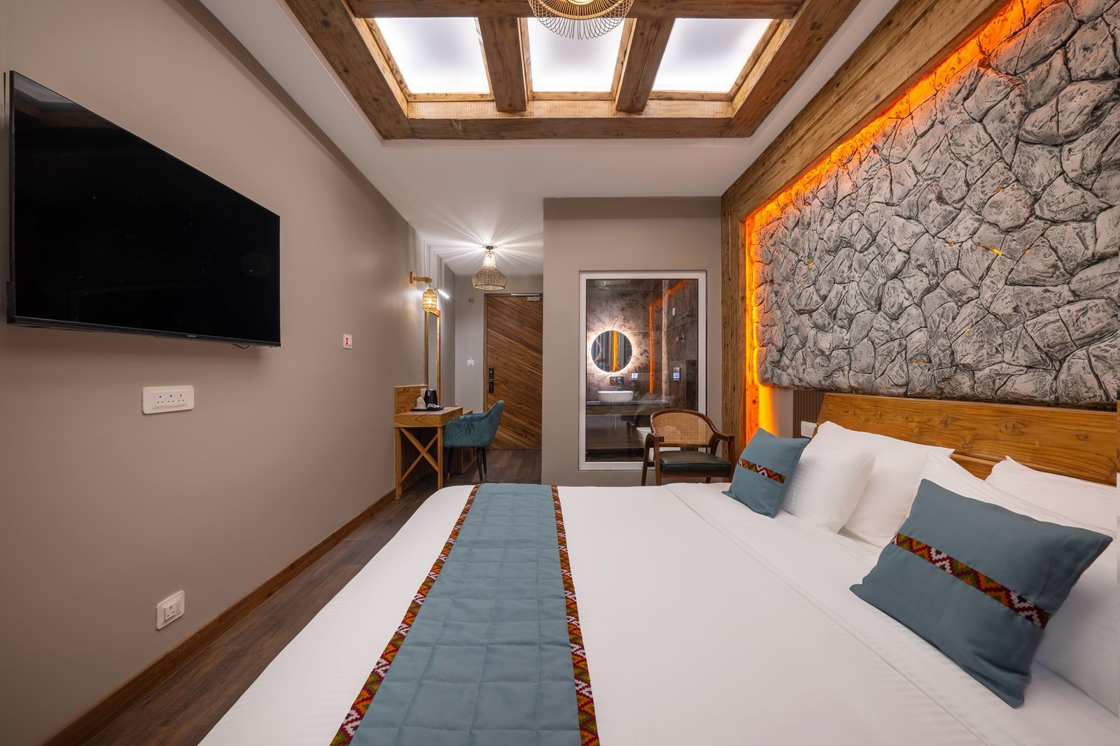 Ett hotellrum med en stor säng, ett skrivbord, en stol, en TV och ett takfönster.
