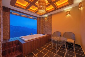 A bathroom with a large window, a bathtub, and two wicker chairs.