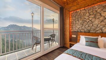 Habitación de hotel con un balcón grande, una cama con colcha y una pared de piedra.