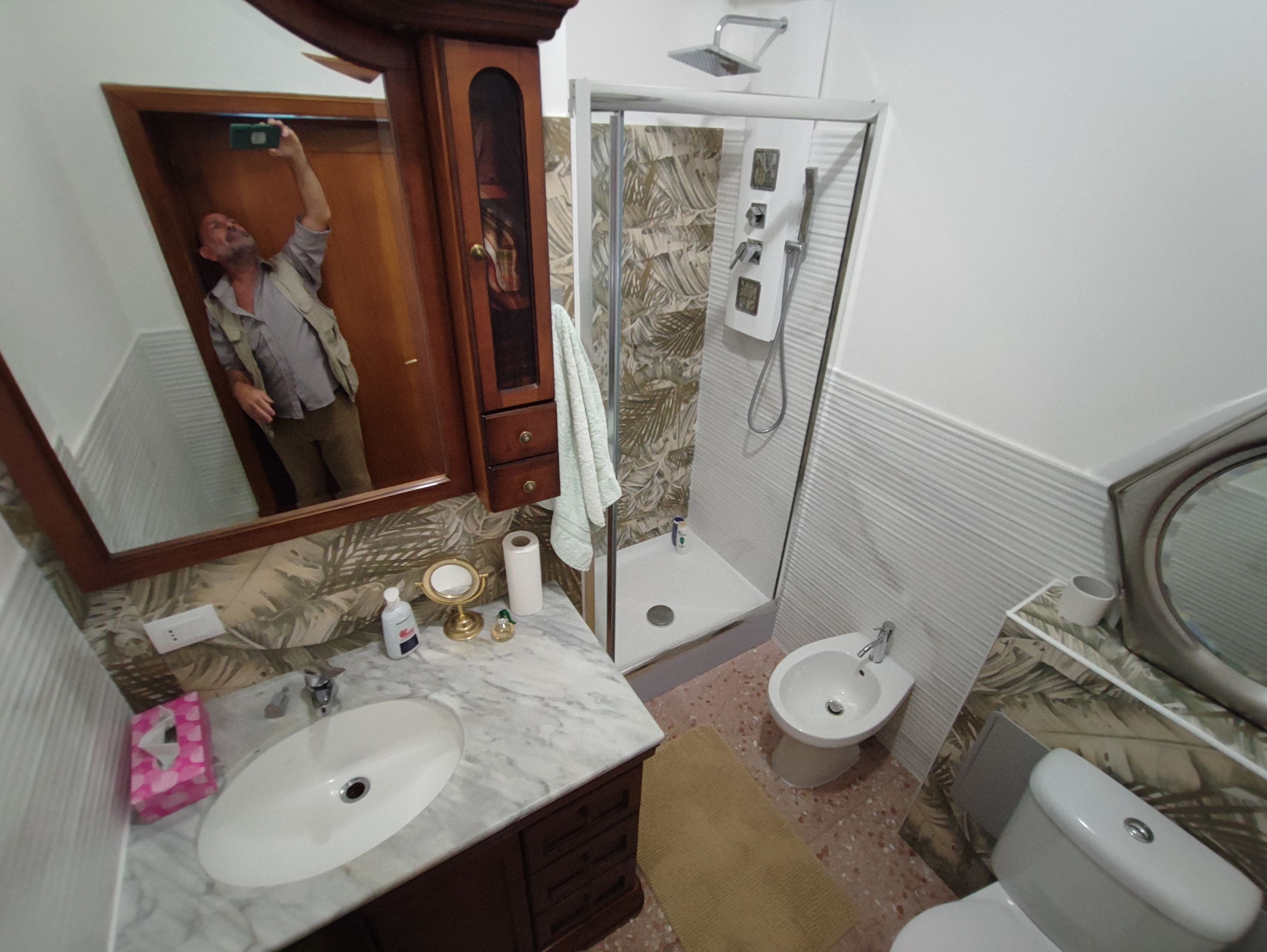 A bathroom with a sink, mirror, vanity, shower, toilet, and a towel rack.