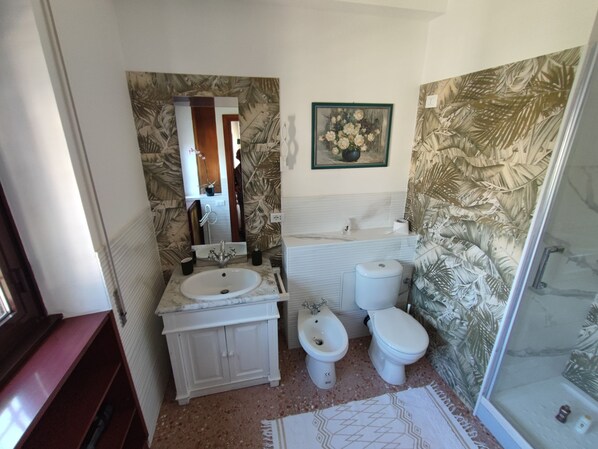 A bathroom with a sink, a bidet, a toilet, and a shower area.