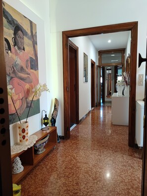 A hallway with a wooden door, a vase with flowers, a decorative lamp, and a painting on the wall.