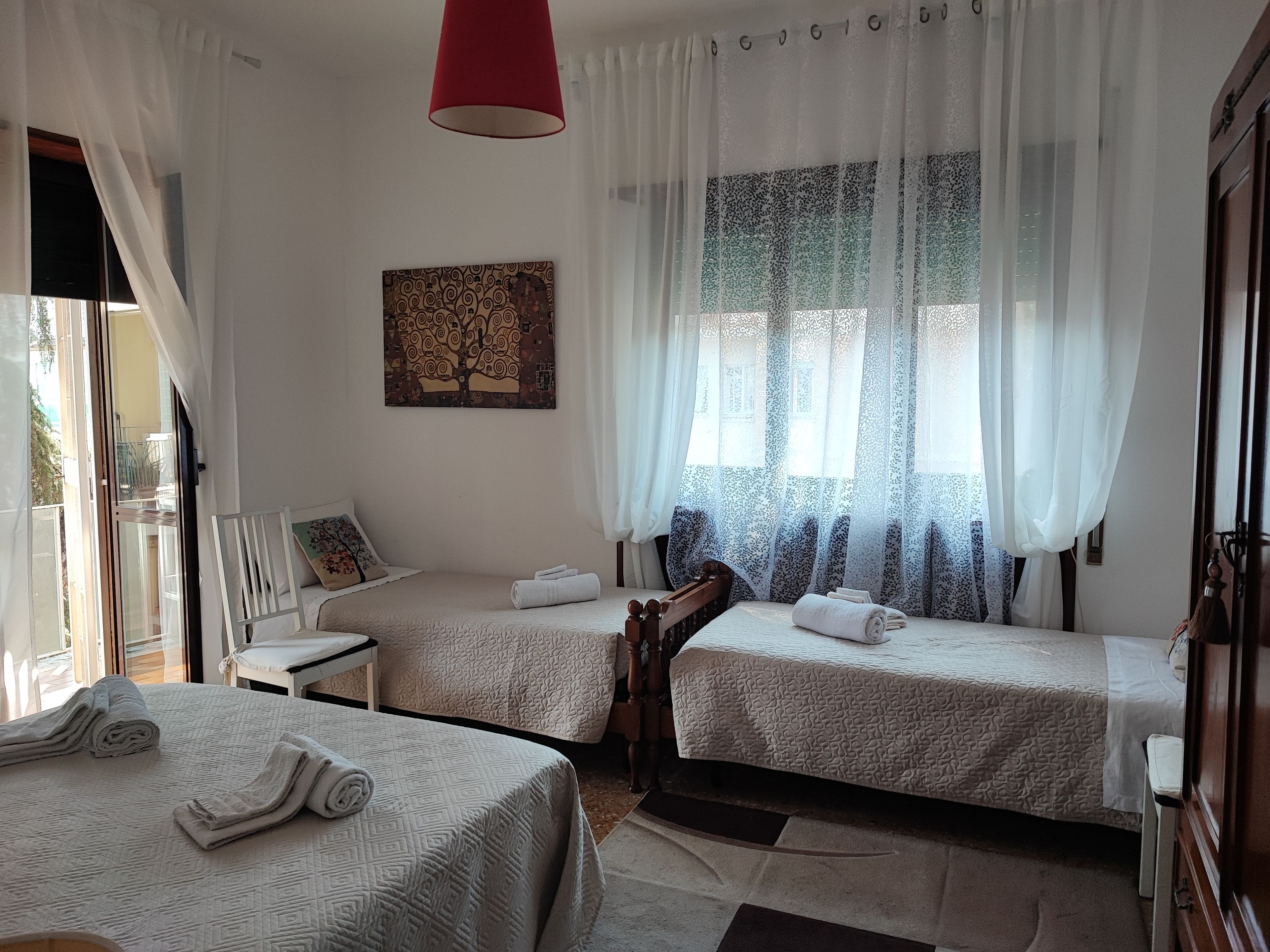 Een hotelkamer met twee bedden, een rode hanglamp, een raam met gordijnen met een patroon en een aan de muur bevestigd schilderij.