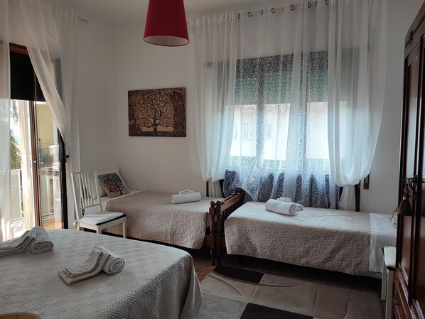 A hotel room with two beds, a red hanging light, a window with patterned curtains, and a wall-mounted painting.