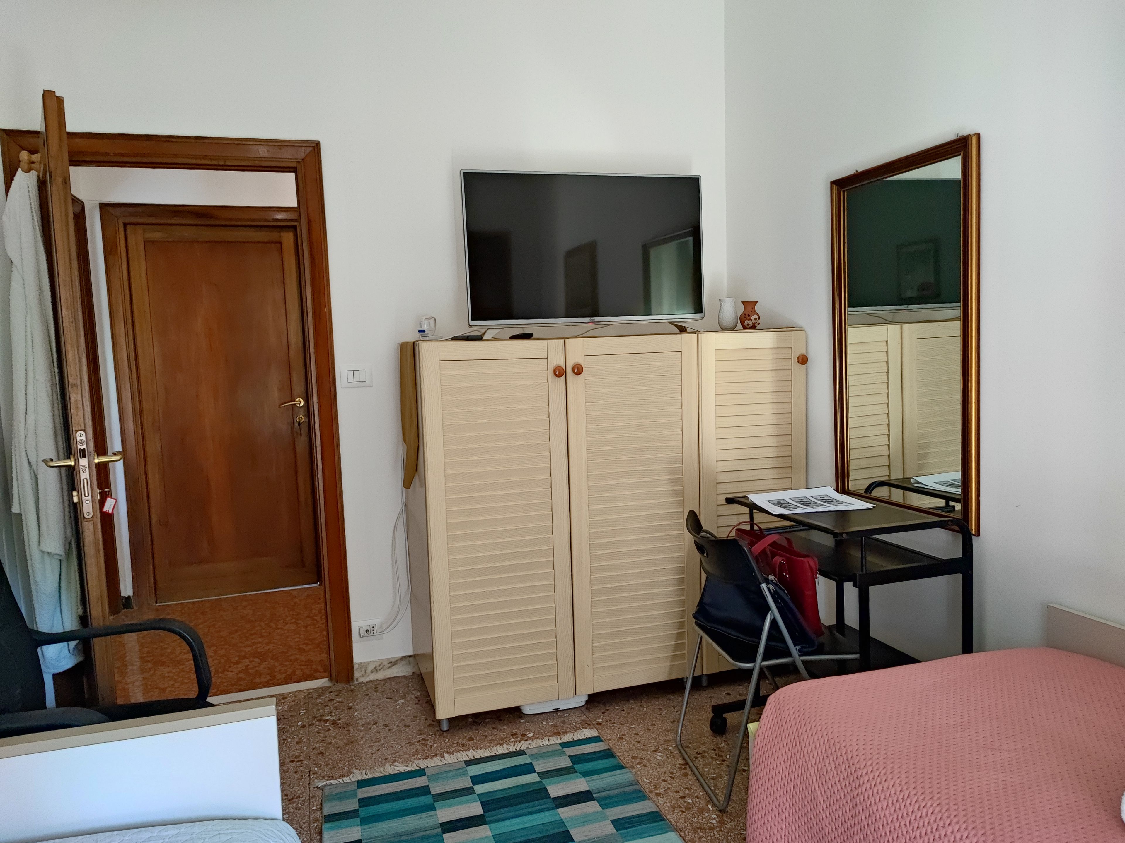 Een kamer met een bed, een bureau met stoel, een garderobe, een televisie en een spiegel.