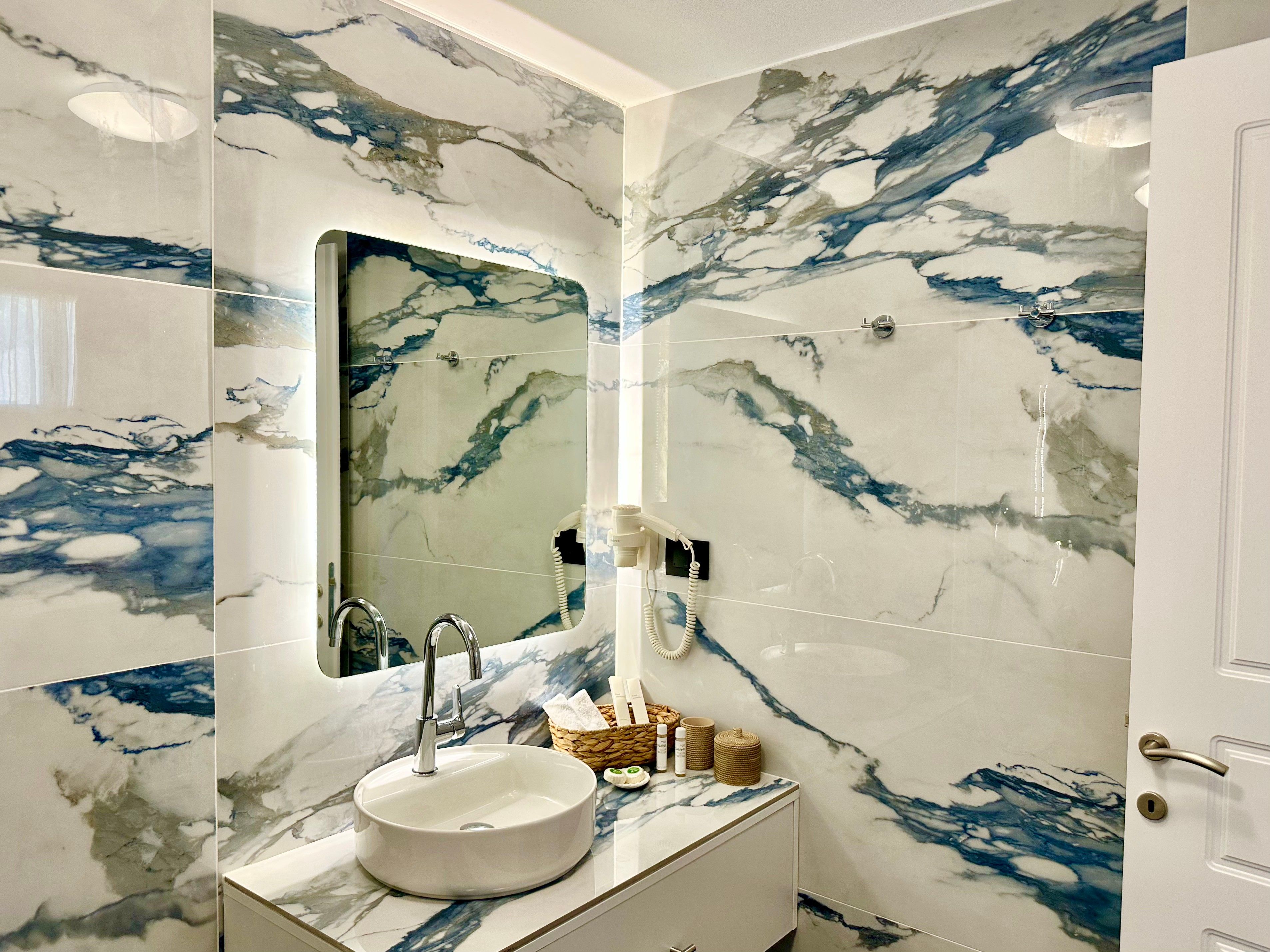 Une salle de bain avec un lavabo en marbre, un miroir et une porte.