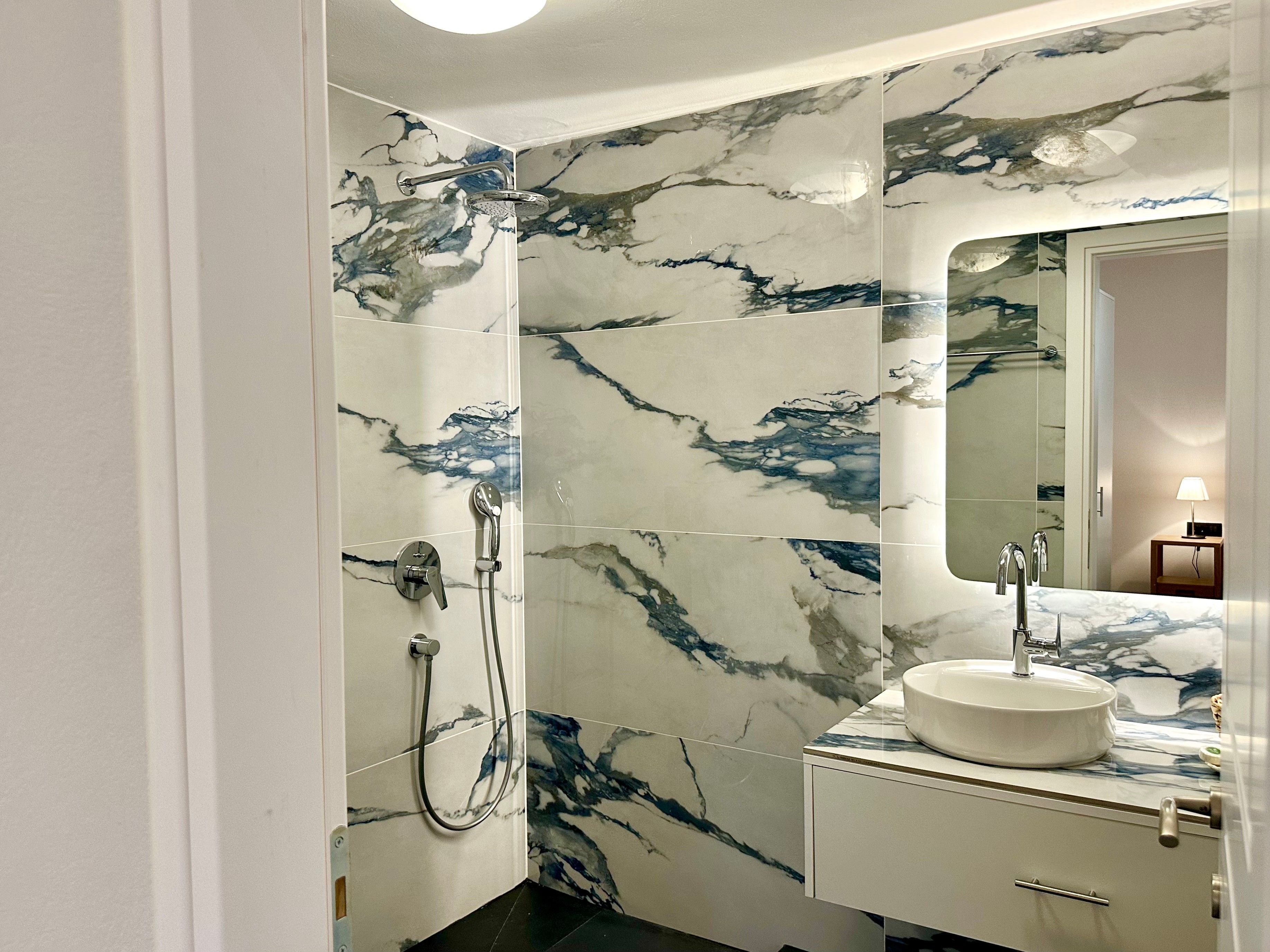 Un baño con ducha de mármol, lavamanos y espejo.
