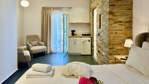 A hotel room with a bed, a chair, a desk with a coffee maker, a stone wall, and a window with curtains. - White & black Suites – Suite Five (Σίφνος)