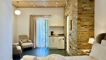 A hotel room with a bed, a chair, a desk with a coffee maker, a stone wall, and a window with curtains.
