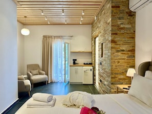Habitació d'hotel amb llit, una cadira, escriptori amb cafetera, paret de pedra i finestra amb cortines.
