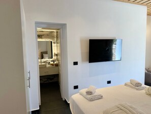 A hotel room with a bed, a TV mounted on the wall, a bathroom with a mirror, and a door leading to another room.