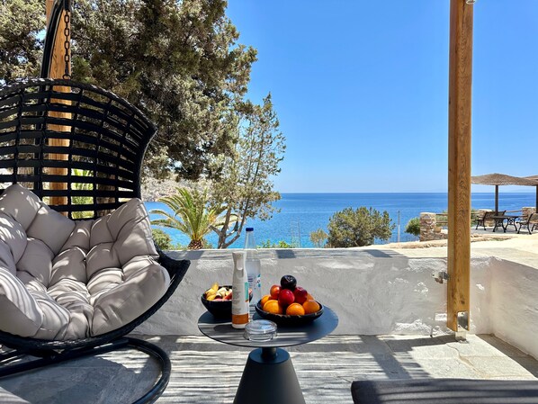 Una cadira de vimet amb seient folrat, una taula amb un plat de fruita i una ampolla, i vista al mar.