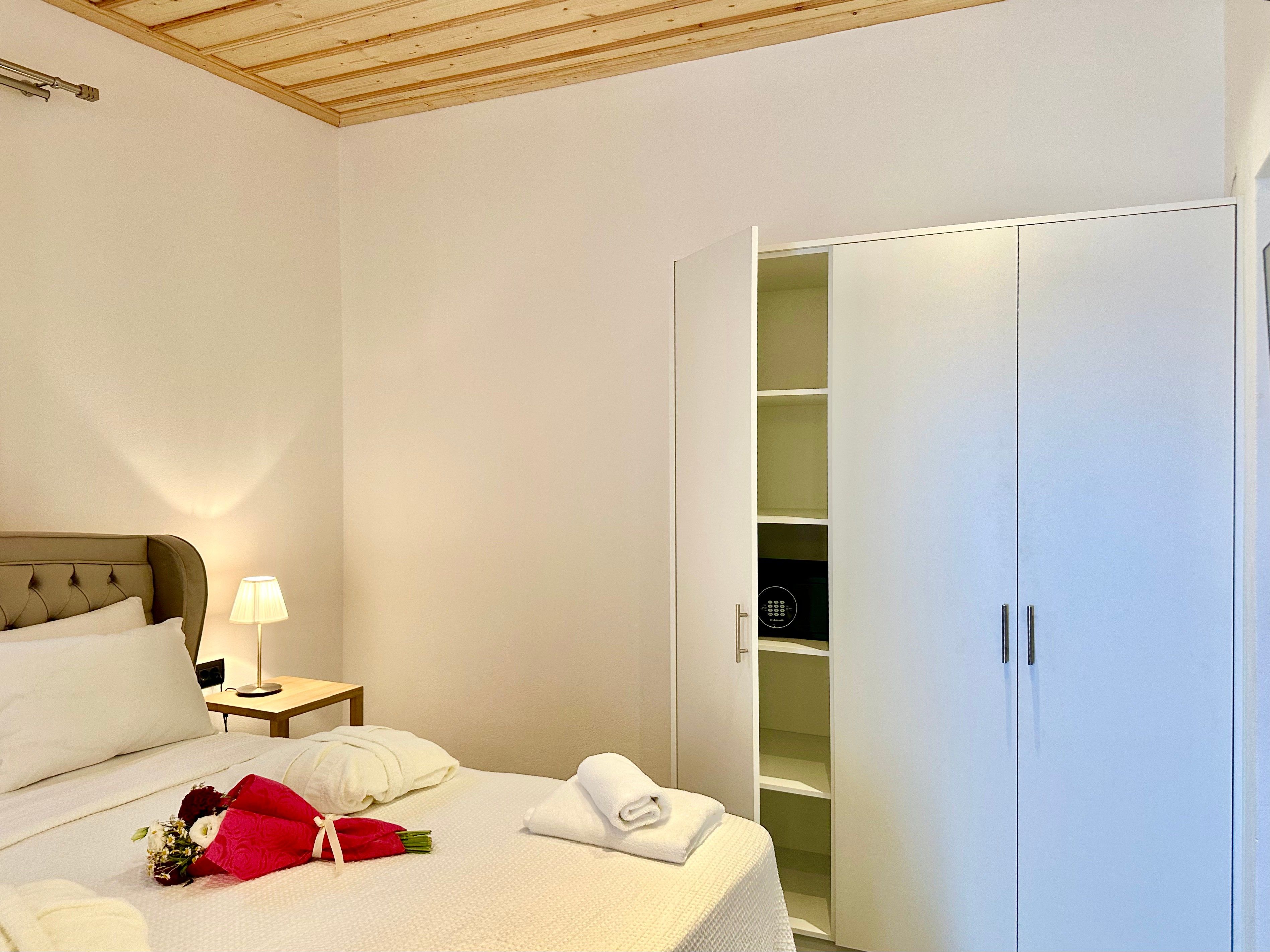 A hotel room with a bed, bedside table, lamp, and a wardrobe with multiple shelves.