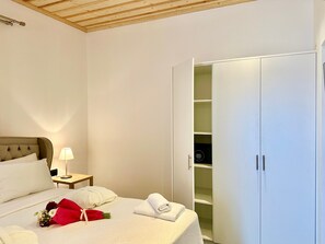 Quarto de hotel com cama, mesa de cabeceira, luminária e armário com várias prateleiras.