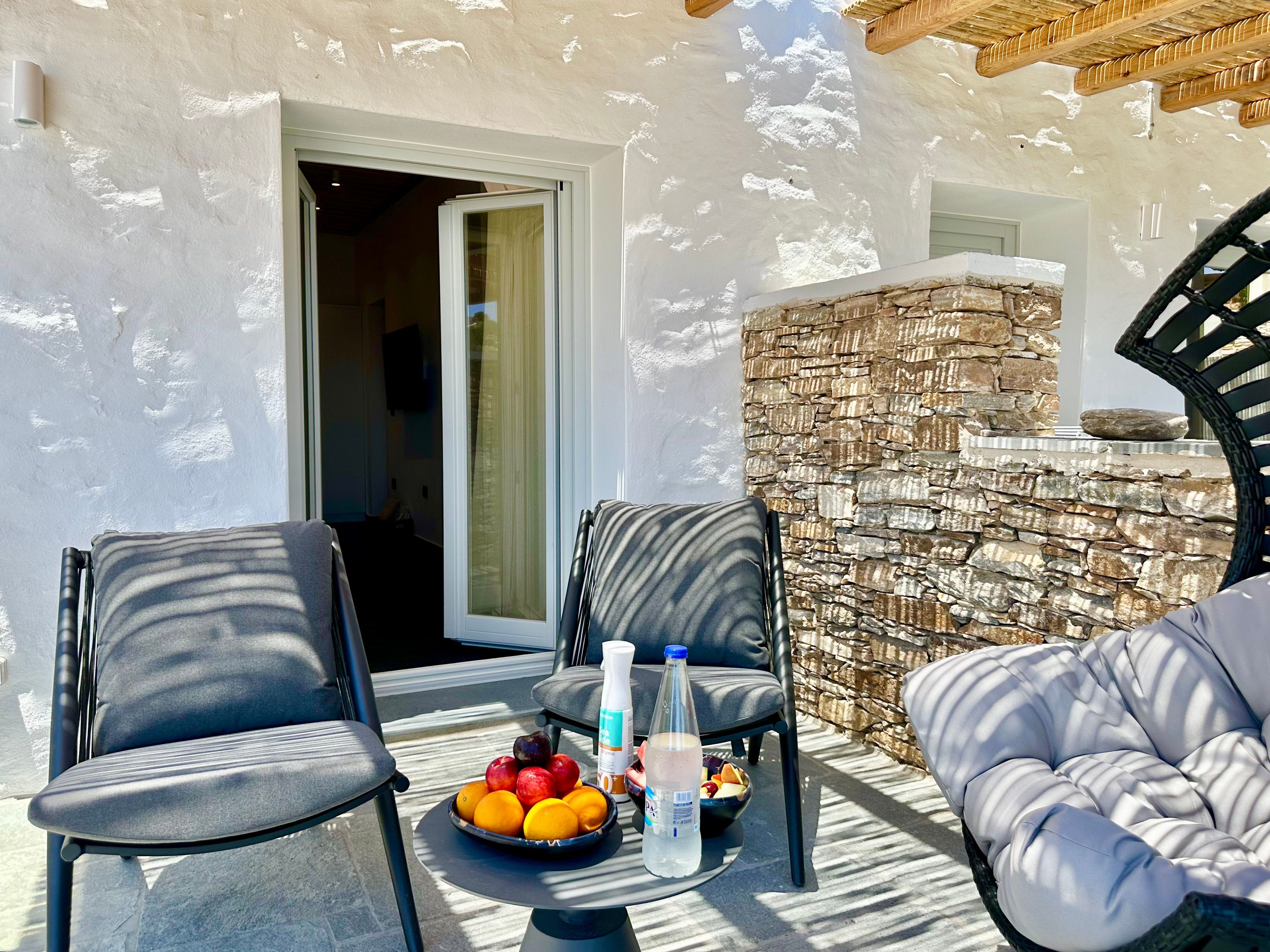 A patio area with two chairs, a table with fruit and drinks, and a stone wall.