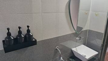 A bathroom with a white sink, a glass shower enclosure, and a black soap dispenser holder.