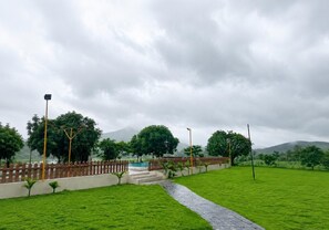 Un camino pavimentado conduce a una cerca de madera y a una zona de piscina con montañas al fondo.