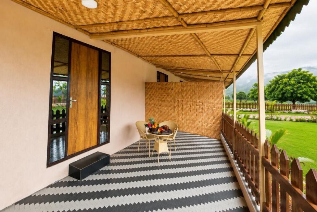A covered balcony with a patterned floor, a table with chairs, and a view of a garden.