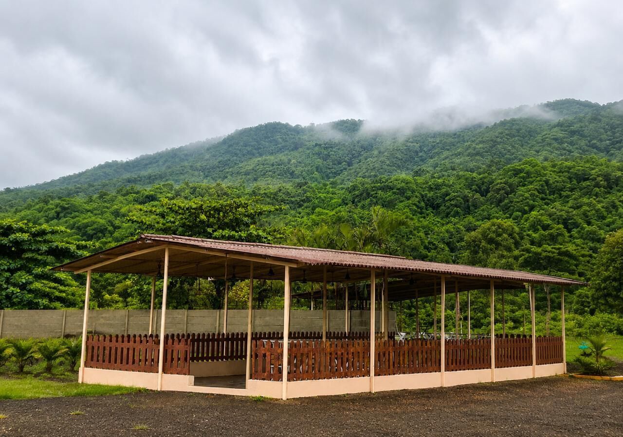 Ein überdachter Pavillon mit Holzzaun, vor einer Kulisse aus saftig grünen Hügeln und bewölktem Himmel.